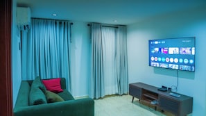 Sala de estar com televisão de tela plana na parede, sofá verde com almofadas e um móvel de entretenimento de madeira.