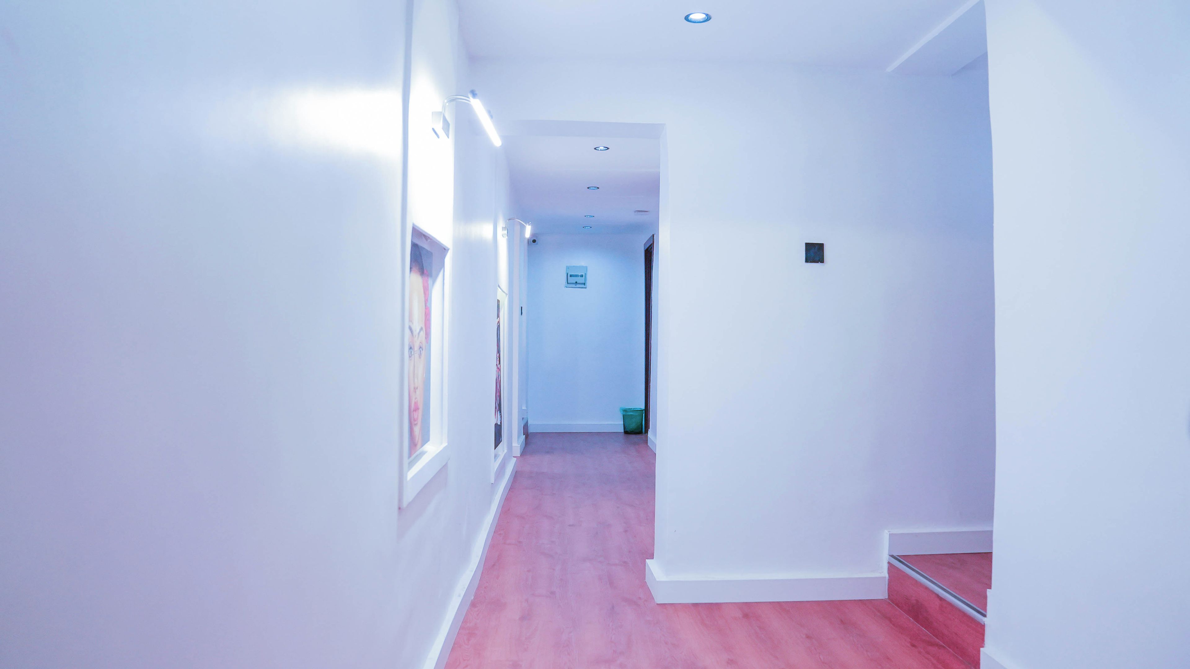 A narrow hallway with white walls and a pink carpet, leading to a door at the end.