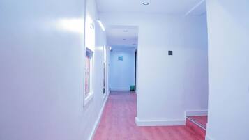 A narrow hallway with white walls and a pink carpet, leading to a door at the end.