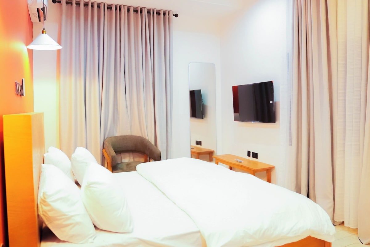 A hotel room with a bed, a chair, a desk, a TV, and curtains.