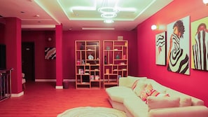 A room with a red carpet, a white sofa, and a bookshelf filled with books and decorative items. - Bluenix Haven Luxury Apartments  (Abuja Municipal)
