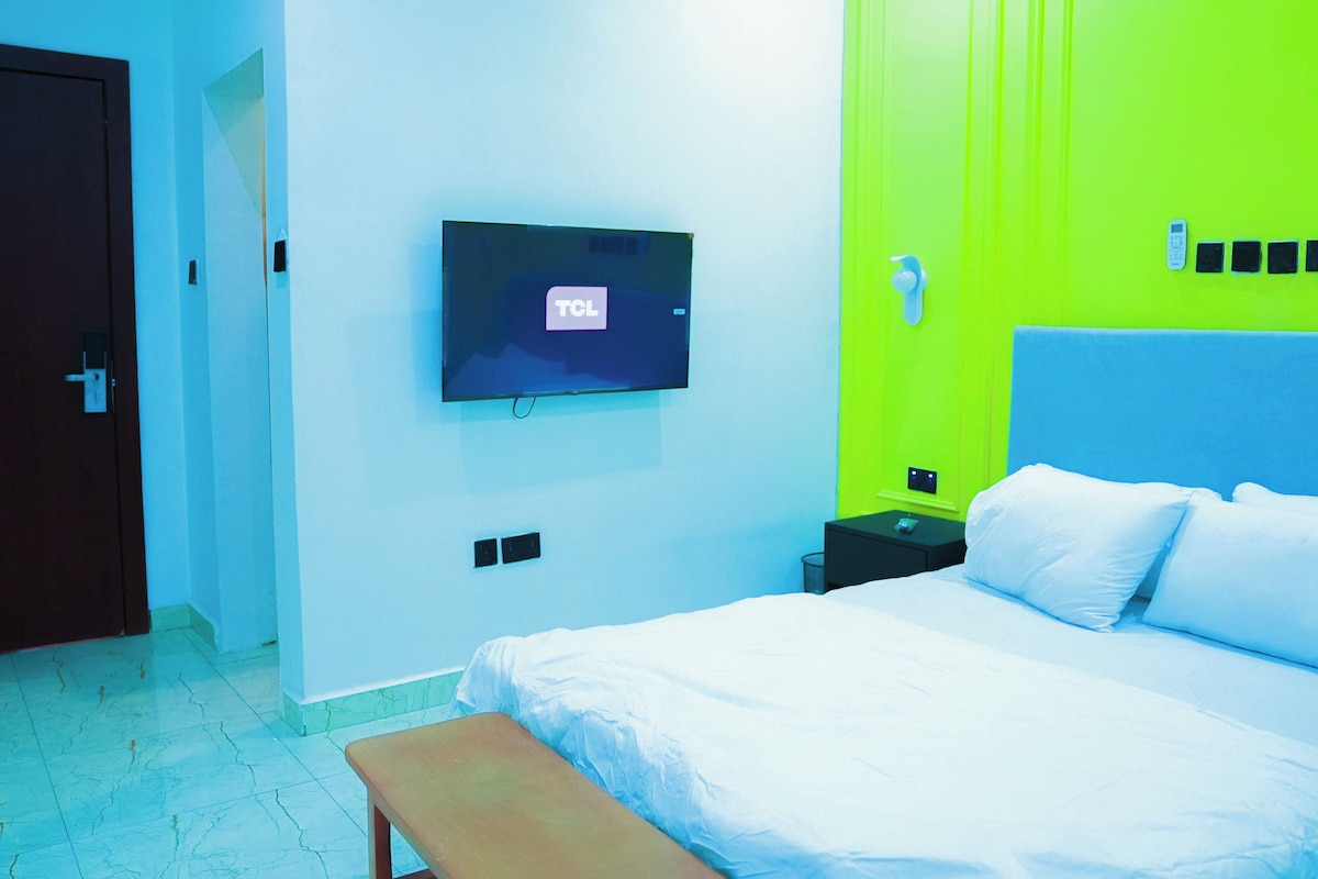 A hotel room with a bed, a television mounted on the wall, a nightstand, and a door.