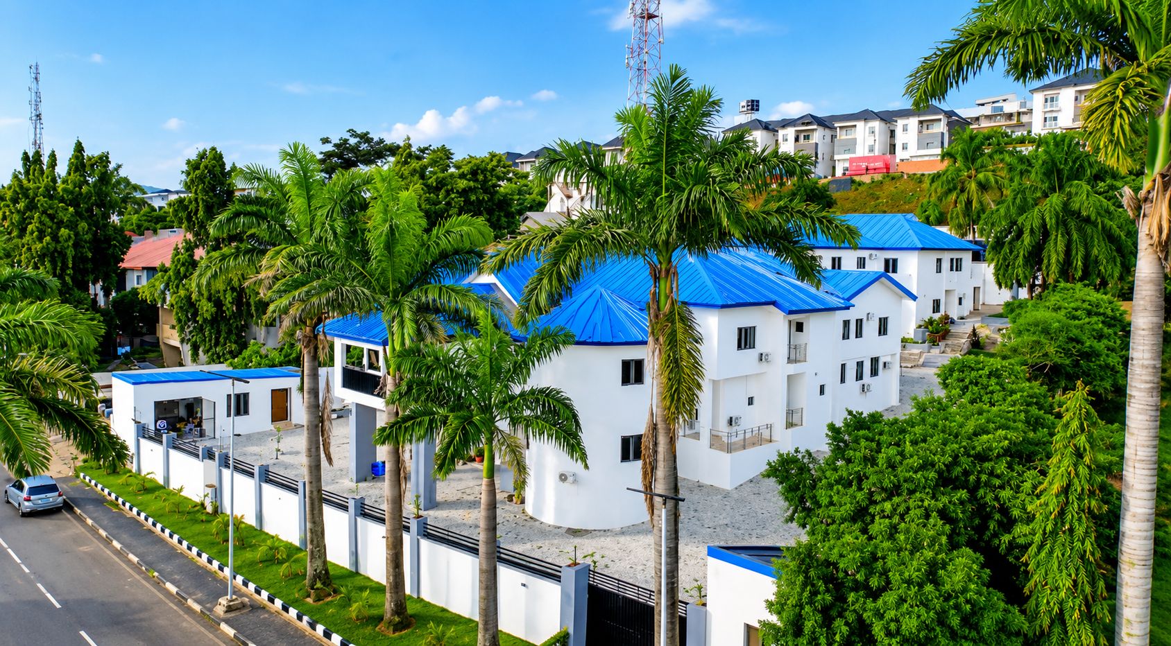 A residential area with white buildings and blue roofs, surrounded by palm trees.