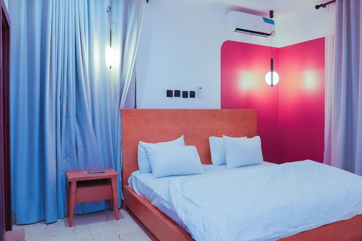 A bedroom with a bed, a nightstand, a wall-mounted air conditioner, and curtains.