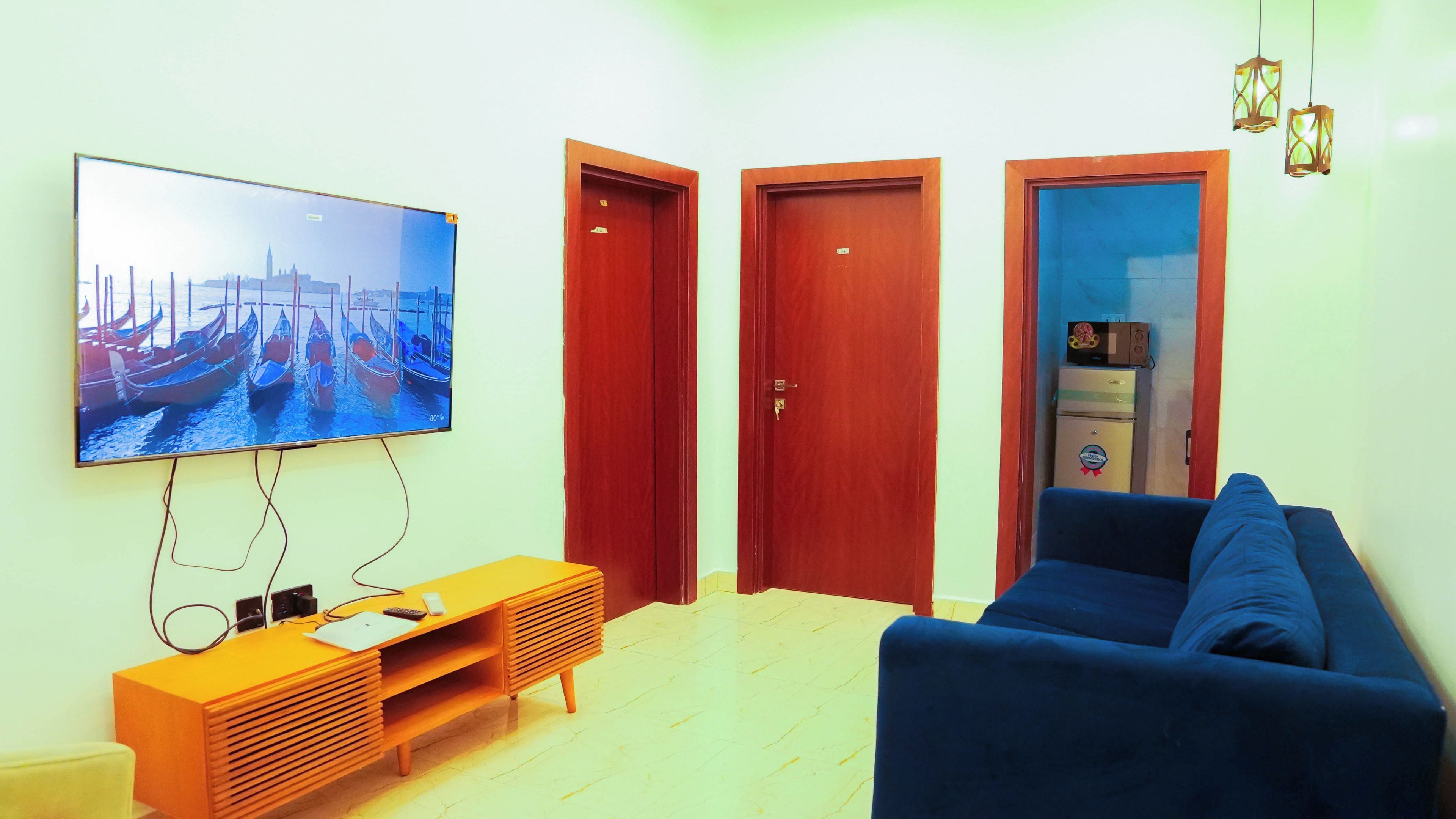 Una sala de estar con televisor, sofá, mueble de madera para entretenimiento y dos puertas.