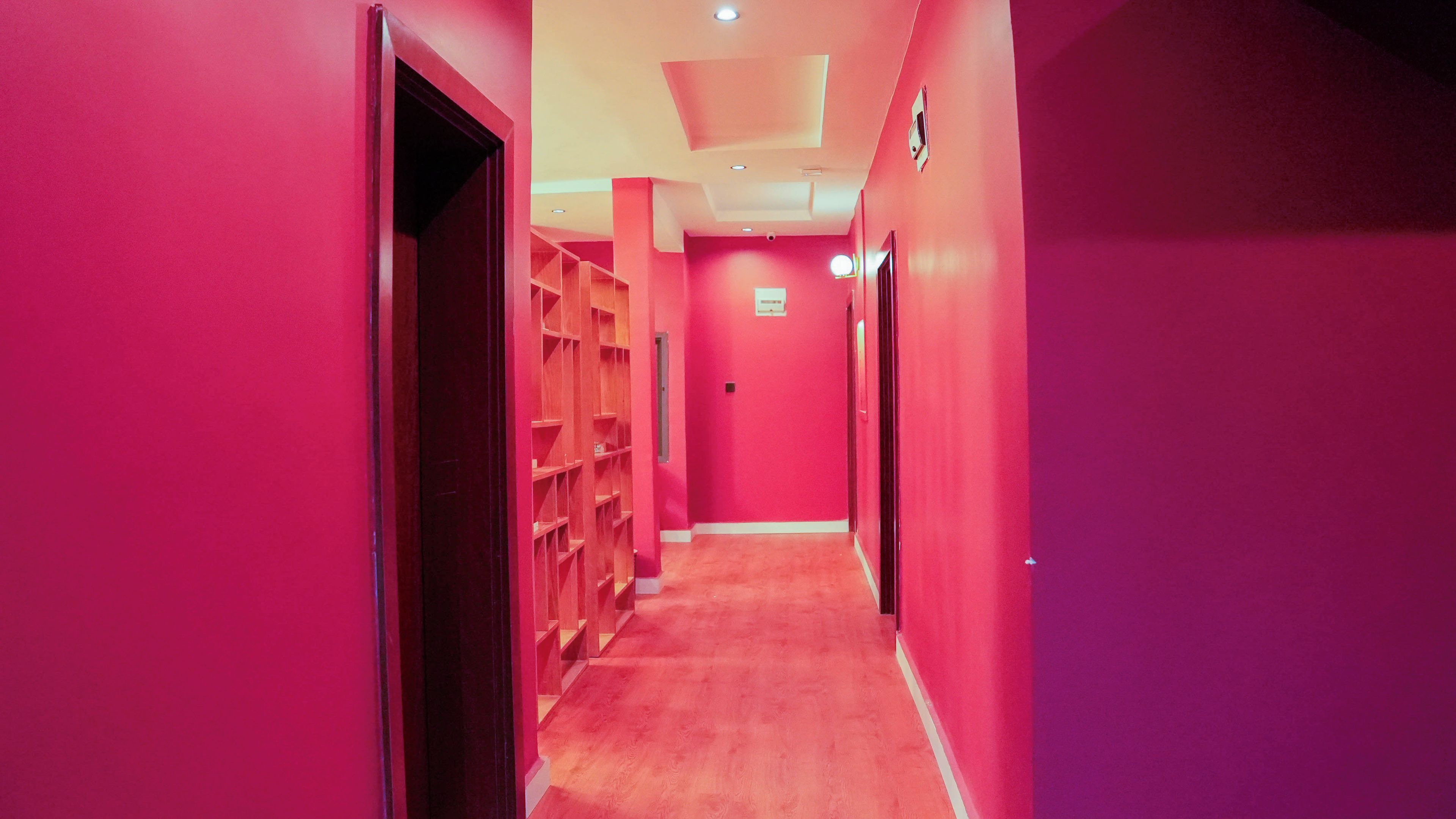 A corridor with pink walls and wooden shelving units.
