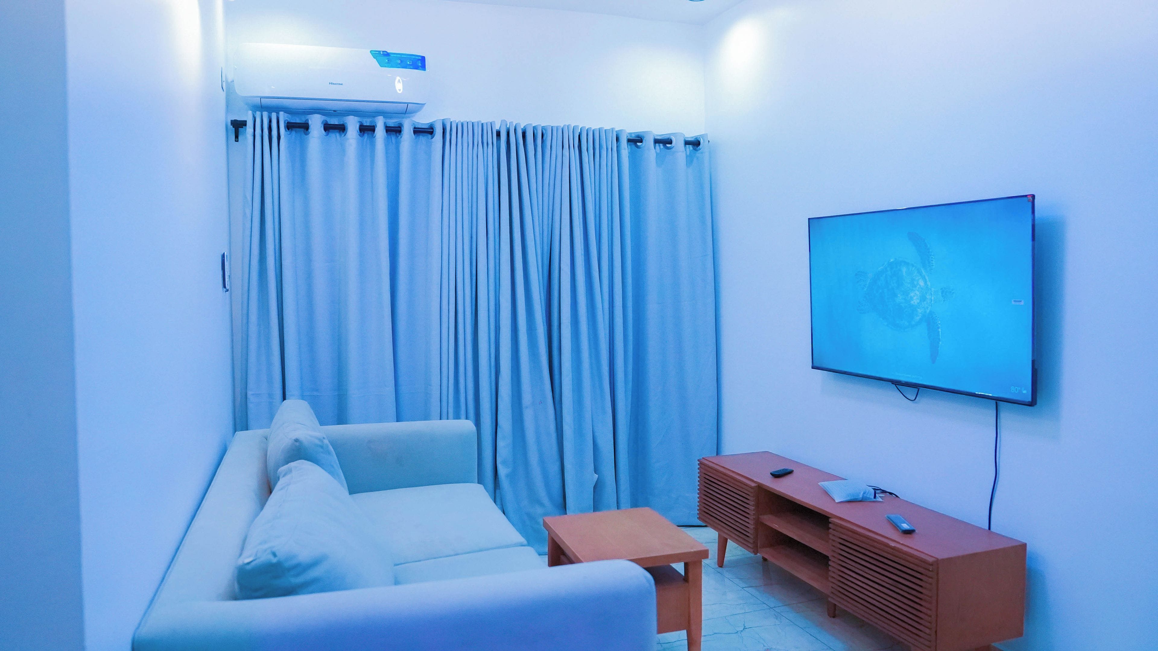 A living room with a sofa, a television mounted on the wall, and a wooden entertainment unit.