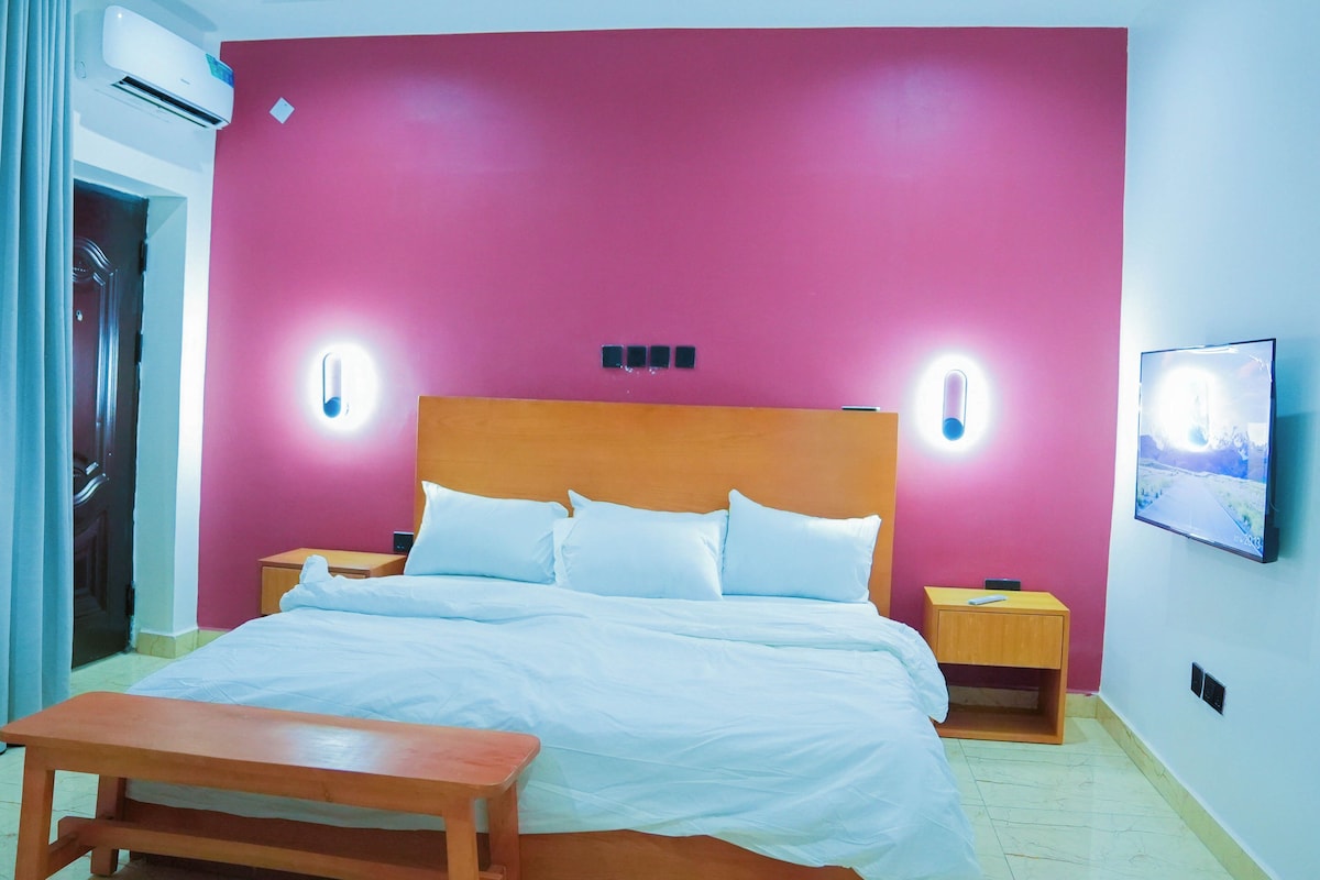 A hotel room with a bed, bedside tables, a bench, and a wall-mounted TV.
