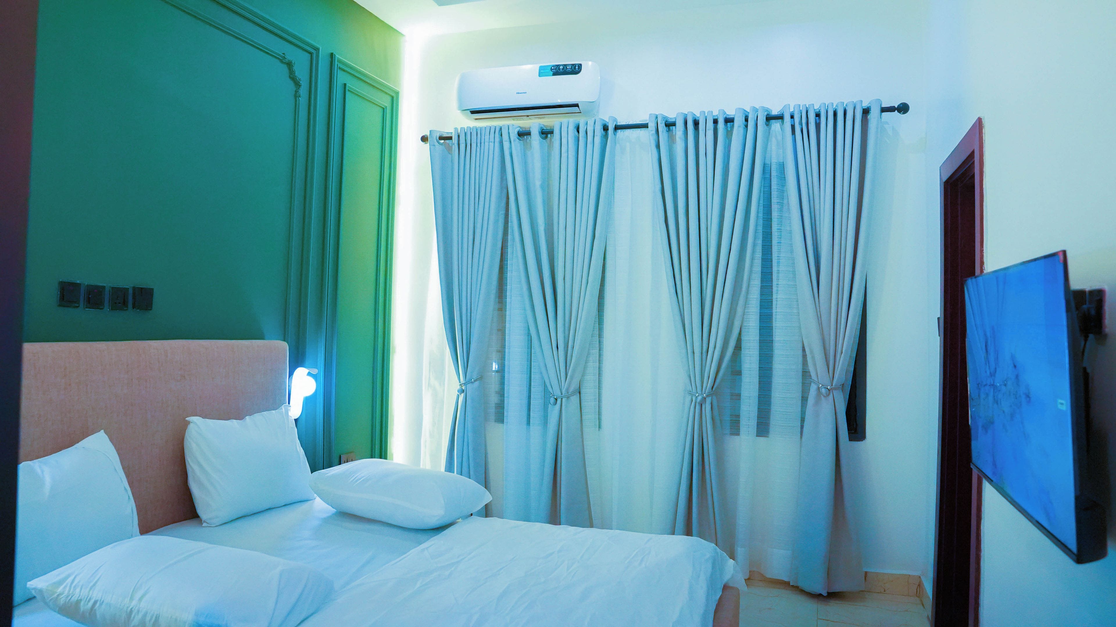 Une chambre d’hôtel équipée d’un lit, de rideaux, d’un appareil de climatisation et d’un téléviseur.