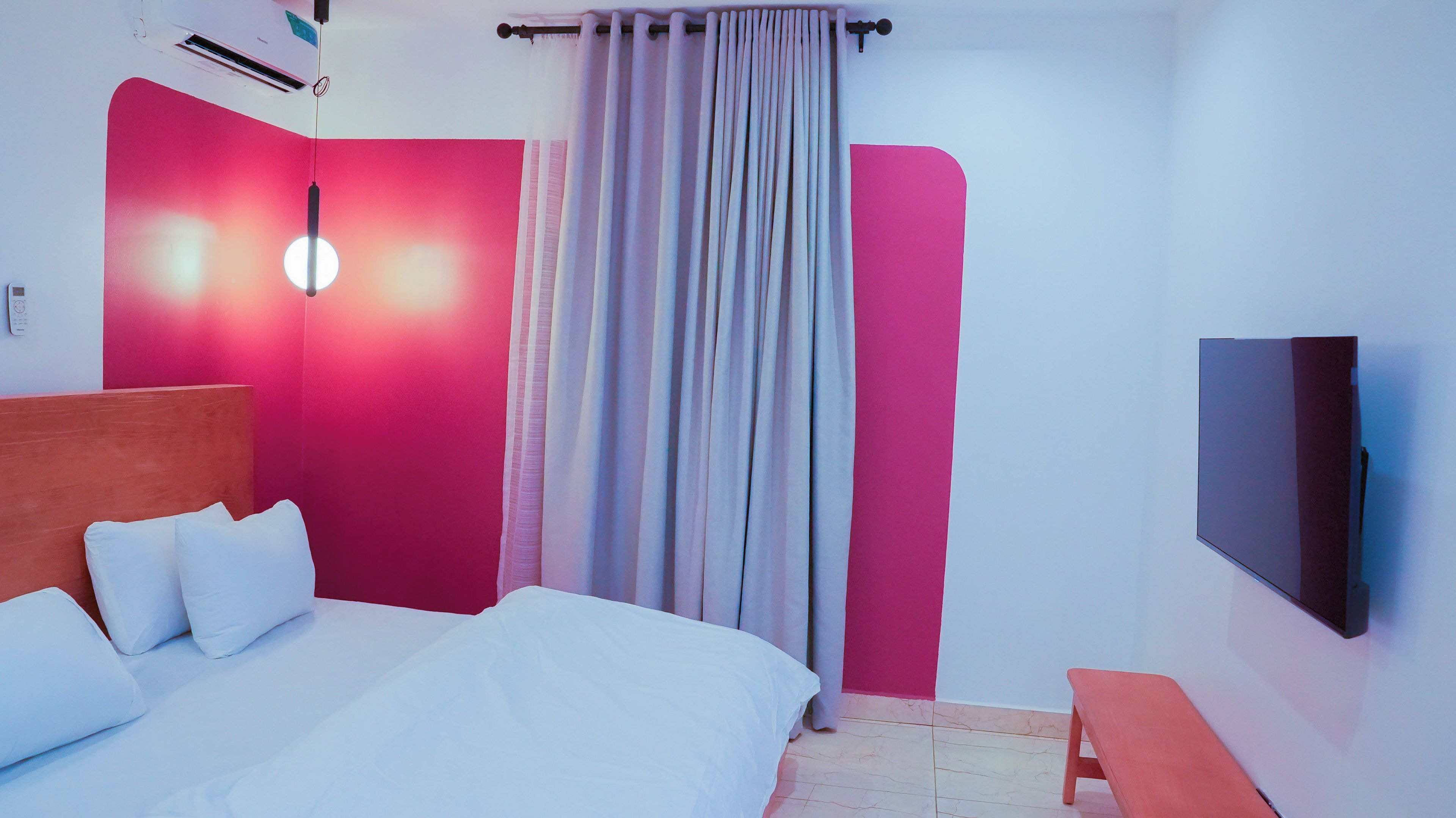 Una habitación de hotel con cama, televisor, mesita de noche y cortina.