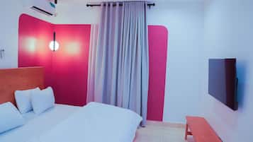 Una habitación de hotel con cama, televisor, mesita de noche y cortina.