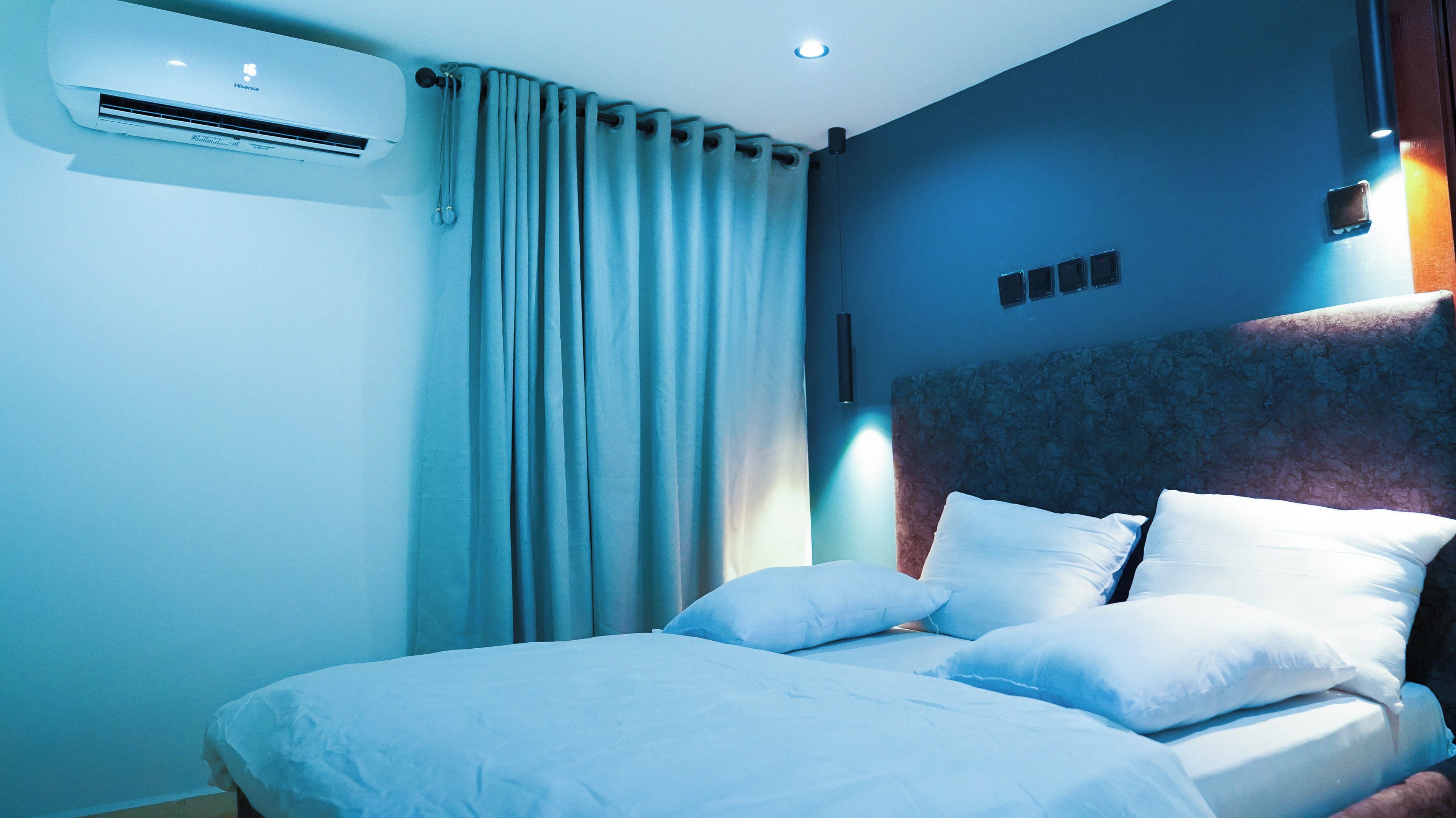 A hotel room with a bed, curtains, an air conditioning unit, and a wall-mounted light fixture.