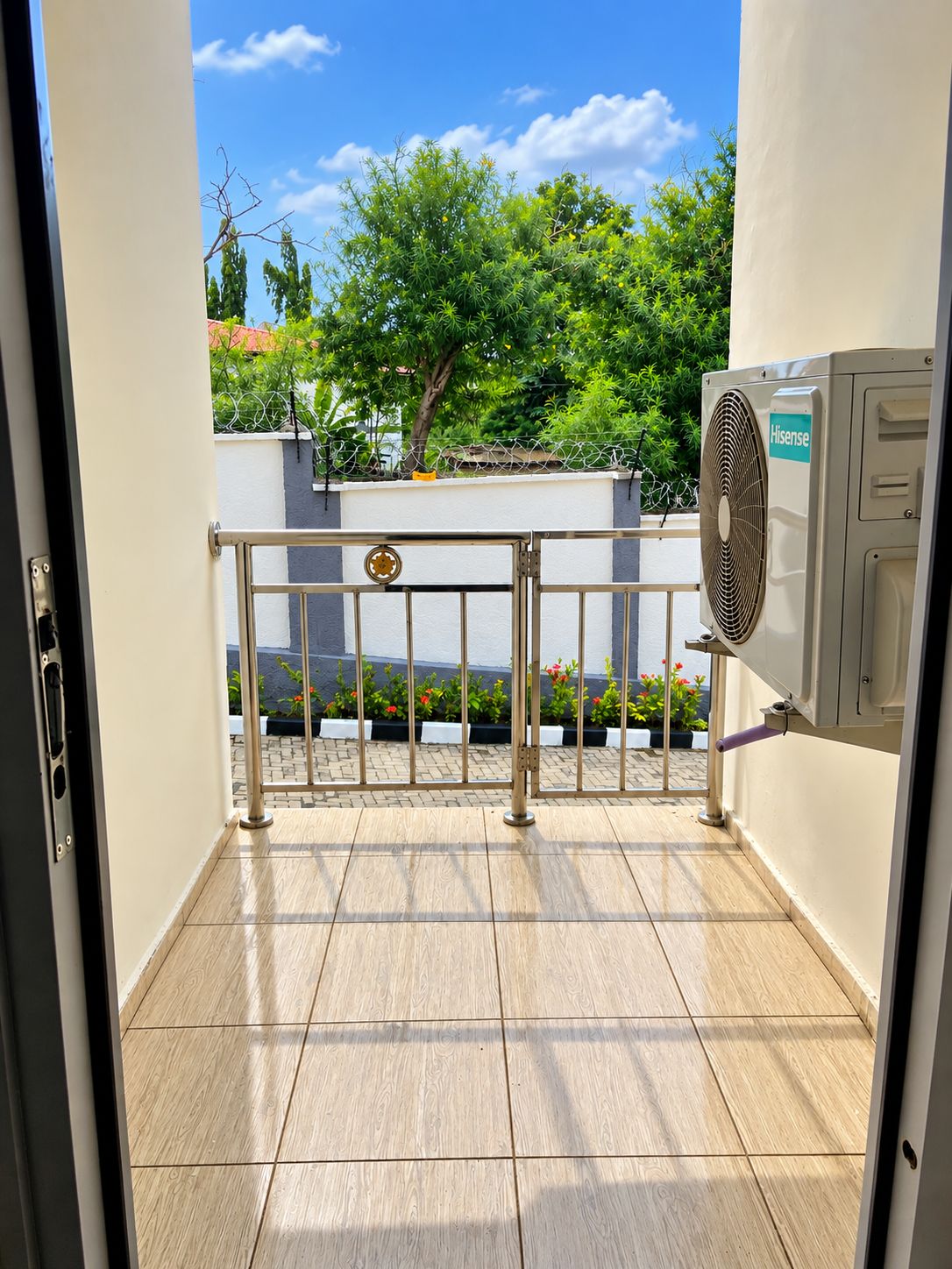 An outdoor area with a metal gate, a fan, and a view of a tree and building in the background.