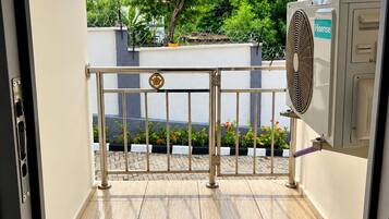 An outdoor area with a metal gate, a fan, and a view of a tree and building in the background.