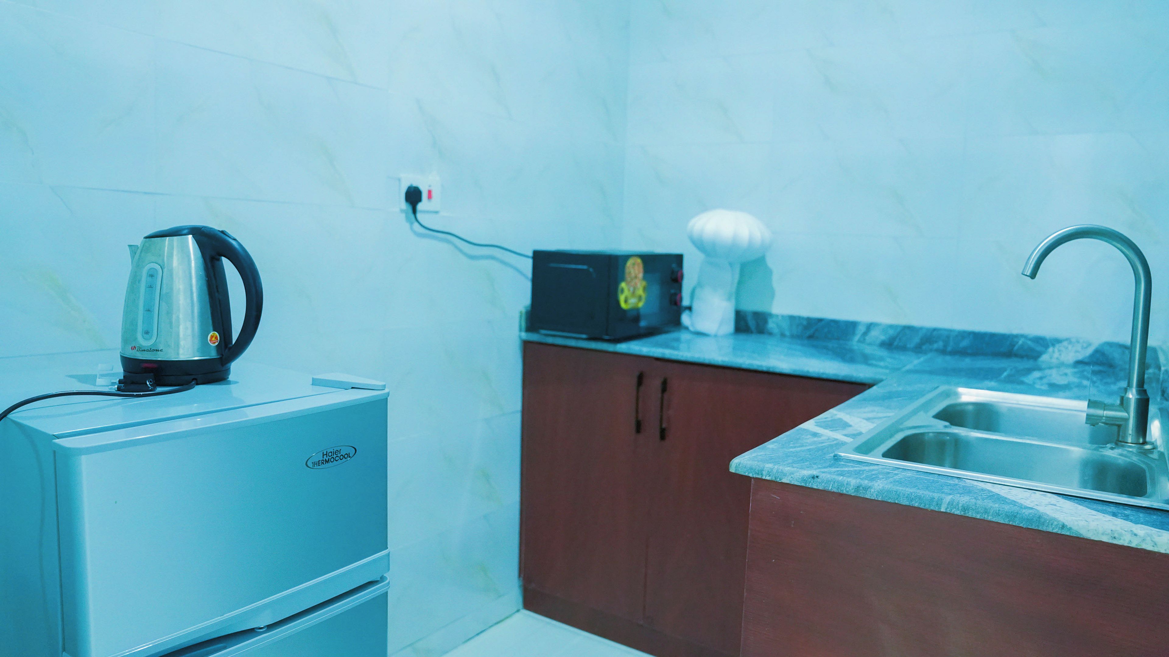 Una cocina compacta con refrigerador, hervidor, tostadora y pileta.