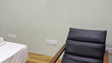 Een kamer met een bed, een houten bankje, een zwarte fauteuil met kussens, en twee kunstwerken in lijsten aan de muur.