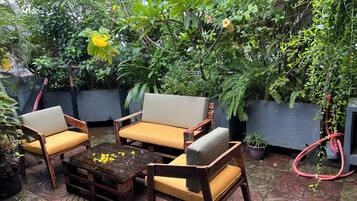 Een buitenruimte met houten meubels en een bijzettafeltje, omgeven door weelderige beplanting en bloempotten.