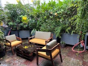 Ein Sitzbereich im Freien mit Holzmöbeln und einem Couchtisch, umgeben von üppigem Grün und Topfpflanzen.