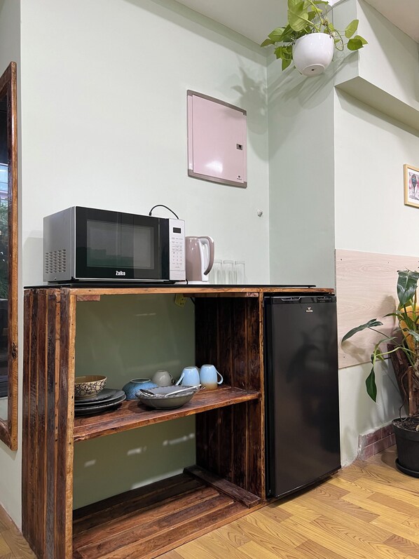 Een kleine keuken met een magnetron, een koelkast en een plank met servies.