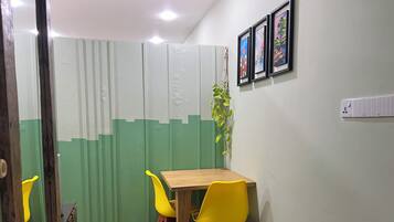 Een kamer met een houten tafel, gele stoelen, een groen-witte scheiding en ingelijste kunstwerken aan de muur.
