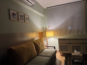 Ein Zimmer mit einer Couch, einer Lampe, einem Fenster und einem Schrank.