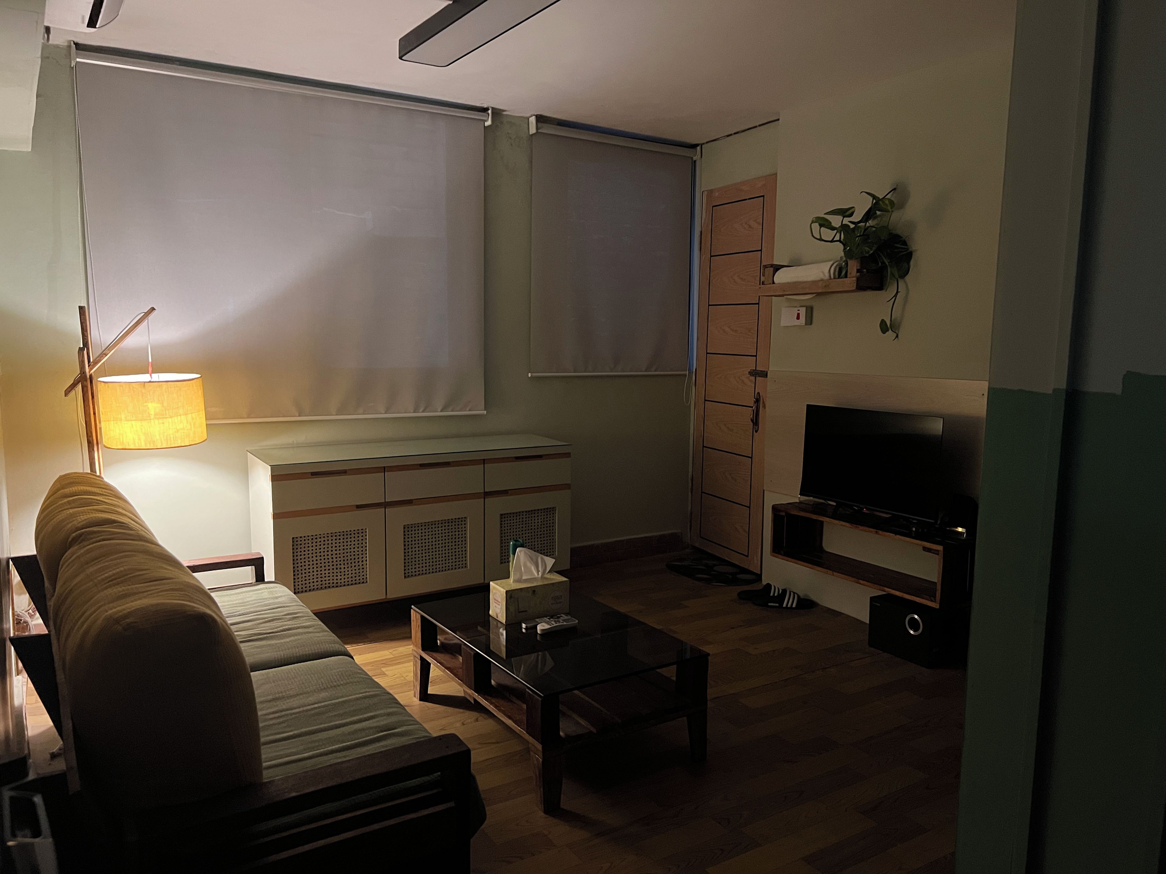 Een woonkamer met een bank, een salontafel, een televisie, een kast en een lamp.