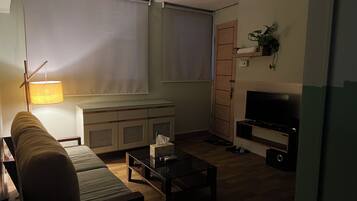 Een woonkamer met een bank, een salontafel, een televisie, een kast en een lamp.
