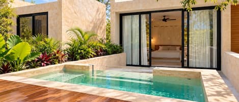 A modern outdoor pool area with a wooden deck, surrounded by lush greenery and a contemporary building with large windows and a sliding door.