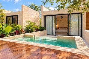 Area piscina moderna all'aperto con un solarium in legno, circondata da vegetazione lussureggiante e un edificio contemporaneo con ampie finestre e una porta scorrevole.