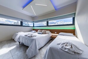 Une chambre d’hôtel moderne avec deux lits, une tête de lit en bois et de grandes fenêtres offrant une vue sur le ciel et les nuages.