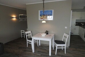 A dining area with a table and chairs, a hanging light fixture, and a wall-mounted picture. - Huus Moorstrand holiday apartment "Moor" (Nordstrand)