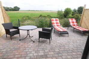 Eine Terrasse im Freien mit einem runden Tisch und vier Stühlen, einer davon mit einem karierten Sitzkissen.