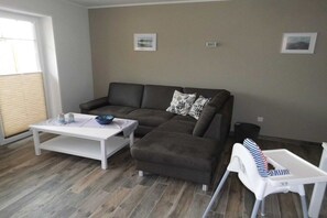 A living room with a brown sectional sofa, a white coffee table, and a white baby changing station. - Huus Moorstrand holiday apartment "Moor" (Nordstrand)