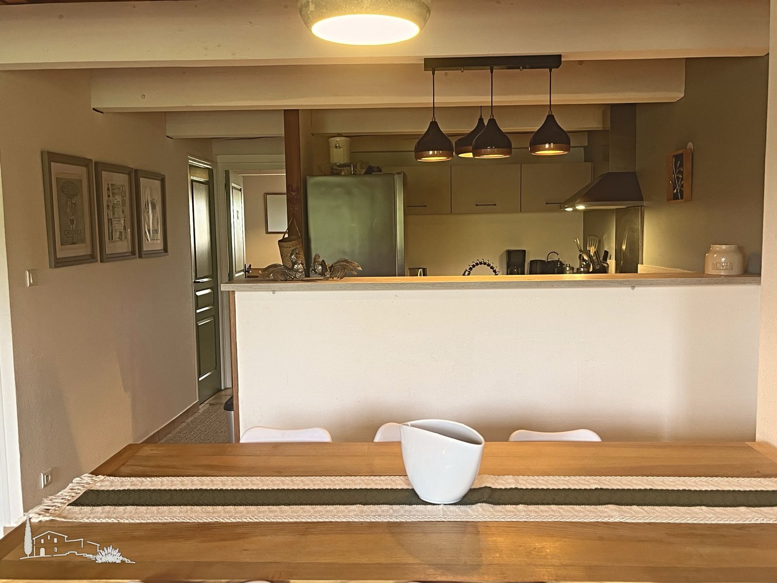 A dining area with a wooden table, a white bowl, and a kitchen in the background.