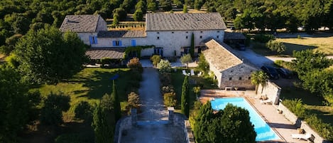 A large stone building with a swimming pool, surrounded by lush greenery and a clear sky.