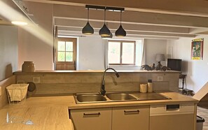Une cuisine dotée d’un plan de travail en bois, d’un évier à deux bacs et de luminaires suspendus.