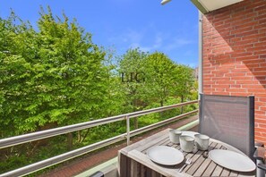 A balcony with a table set for dining, overlooking a lush green landscape. - Holiday apartment Dorfschatz (Langeoog)