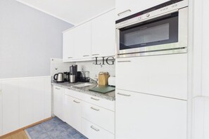 A kitchen with white cabinets, a stainless steel oven, and a coffee maker on the counter. - Holiday apartment Dorfschatz (Langeoog)
