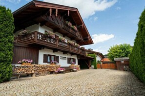 A traditional chalet with a wooden balcony, a stone facade, and a cobblestone driveway. - Holiday apartment with 1 bedroom (Bad Wiessee)