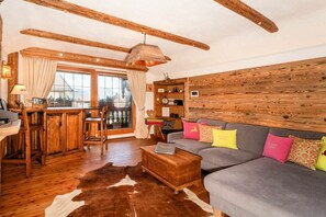 A rustic interior with a wooden ceiling, a sofa with colorful cushions, a cowhide rug, and a wooden bar area. - Holiday apartment with 1 bedroom (Bad Wiessee)
