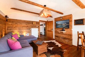A cozy room with a wooden ceiling, a sofa with colorful cushions, a small wooden table, and a cowhide rug. - Holiday apartment with 1 bedroom (Bad Wiessee)