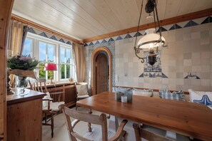 A wooden dining table with chairs, a window with curtains, and a tiled wall with a decorative pattern. - Loddis Leev - Kampen (Sylt) (Kampen (Sylt))