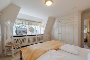 A bedroom with a bed, a vanity with a mirror, a window with curtains, and a wardrobe. - Loddis Leev - Kampen (Sylt) (Kampen (Sylt))