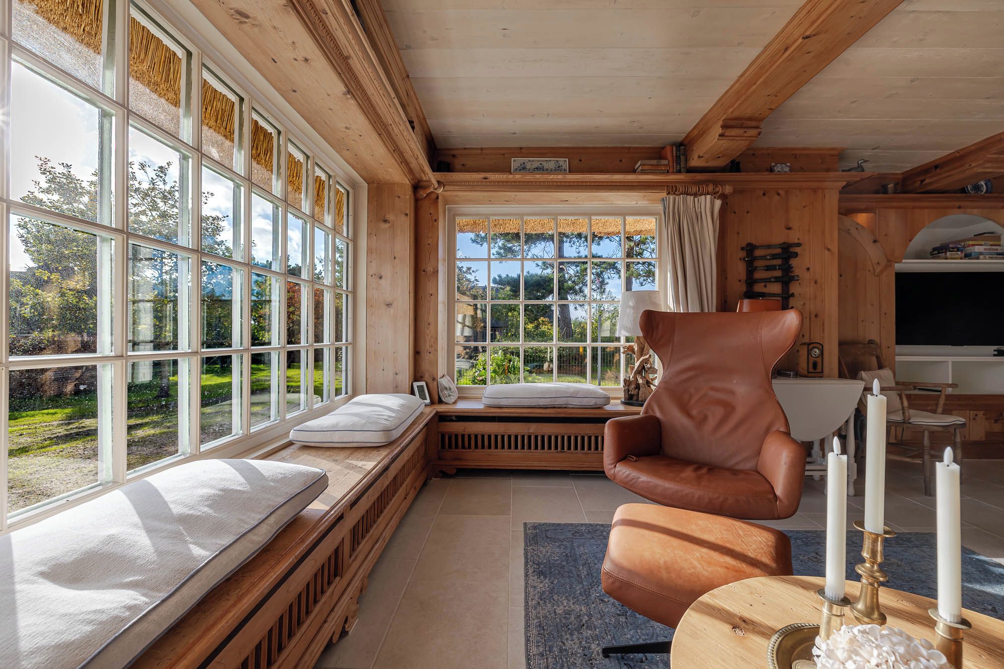 Ein gemütliches Blockhaus-Interieur mit einem großen Fenster, einem Ledersessel, einem Bett mit Matratze und einem Fernseher.