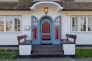 A building with a white facade, a blue door with red accents, and a small porch with benches. - Loddis Leev - Kampen (Sylt) (Kampen (Sylt))