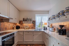 A modern kitchen with white cabinetry, a stone backsplash, a built-in oven, and a variety of appliances including a toaster and coffee maker. - Loddis Leev - Kampen (Sylt) (Kampen (Sylt))