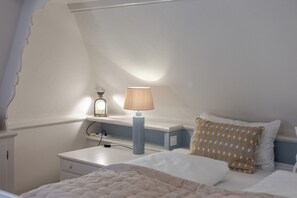 A bedroom with a bed, a bedside table, a lamp, and a patterned pillow. - Loddis Leev - Kampen (Sylt) (Kampen (Sylt))