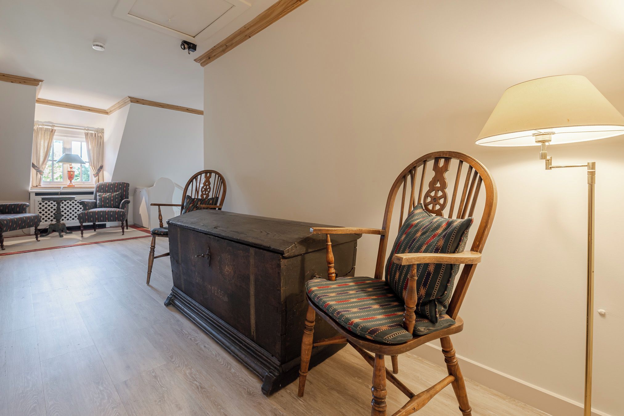 Une pièce avec une chaise en bois, un meuble sombre en bois et un lampadaire.