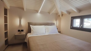 Un dormitorio con cama, mesitas de noche, una ventana y un techo con vigas a la vista.