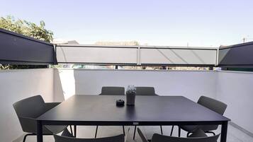 Un patio al aire libre con una mesa, sillas, una planta en maceta y vista a edificios al fondo.